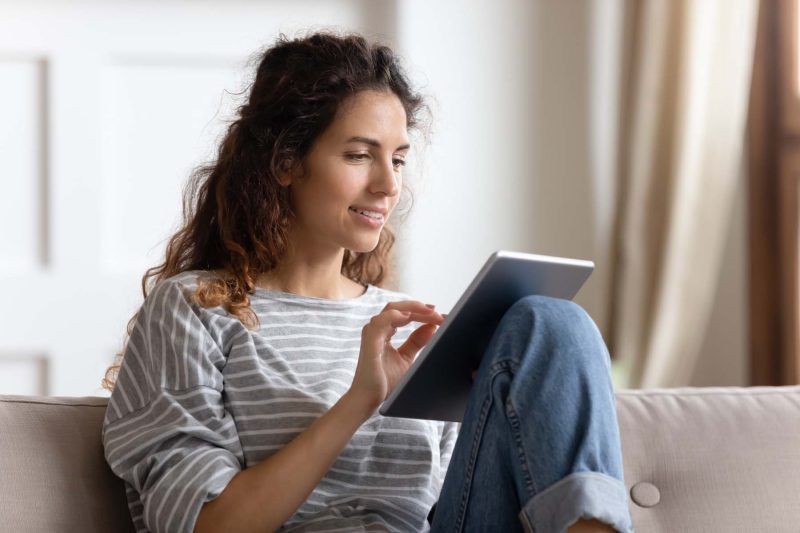 Smiling woman using tablet on couch.