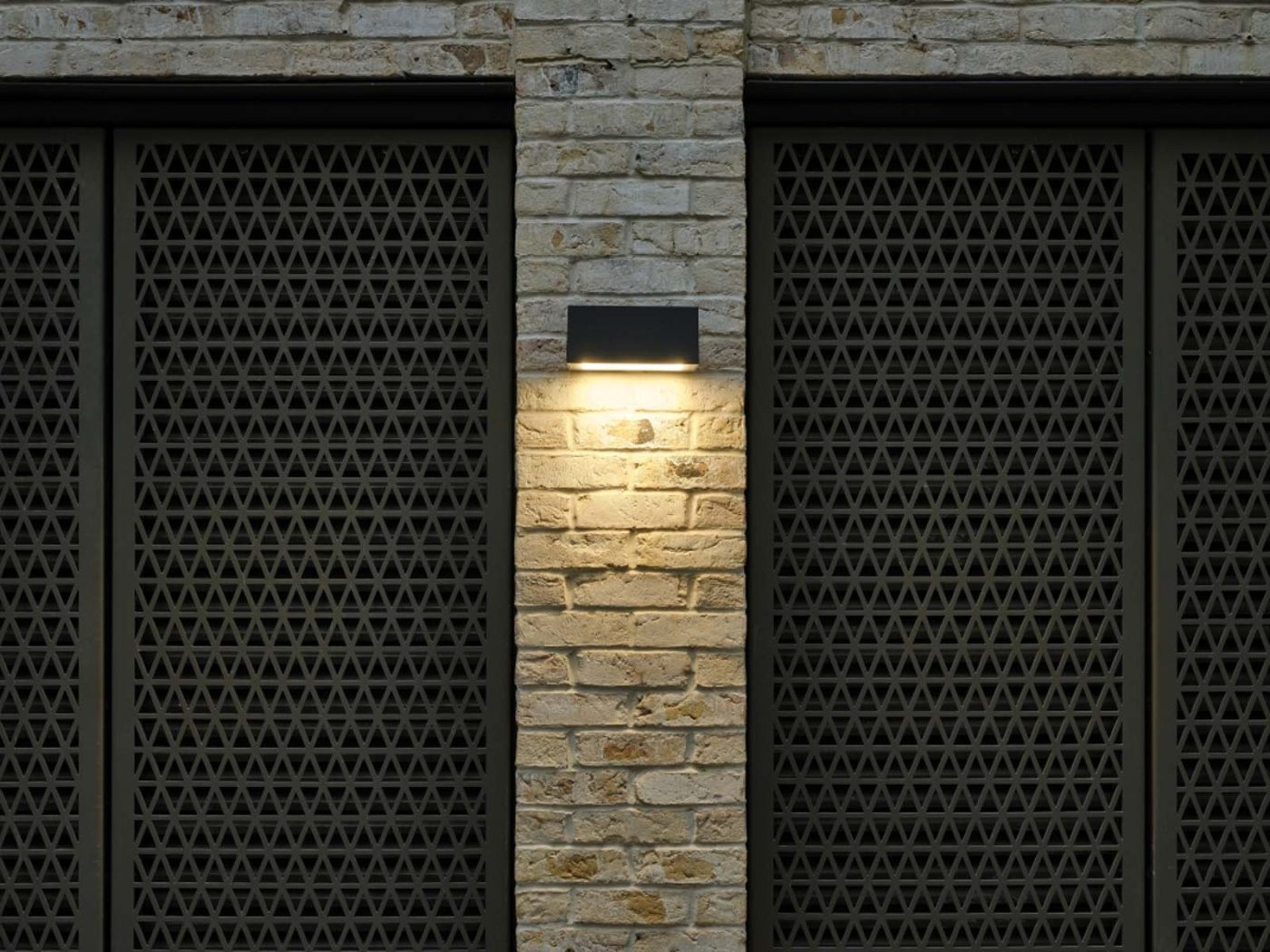 Lit wall-mounted light between dark metal screens.