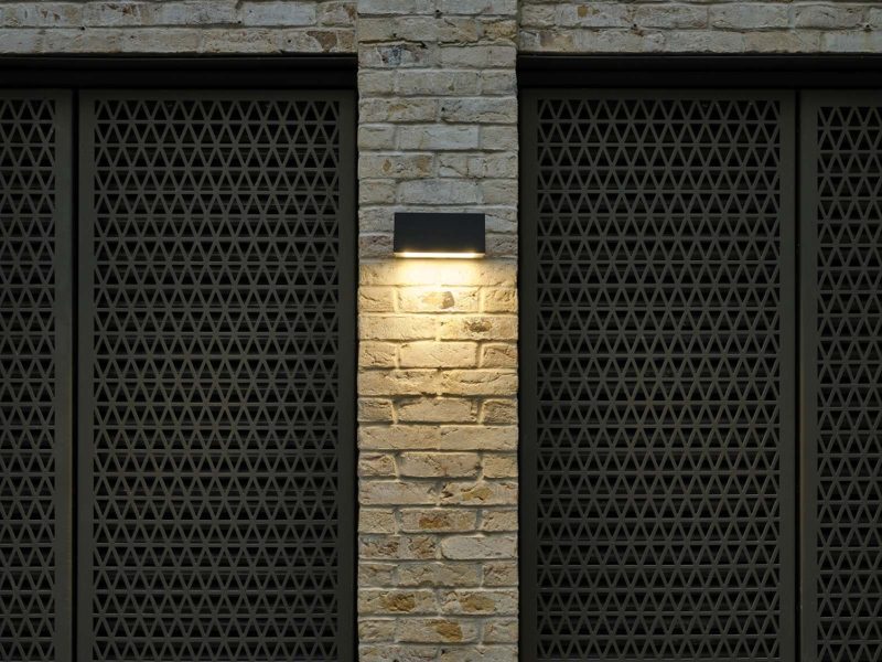Lit wall-mounted light between dark metal screens.