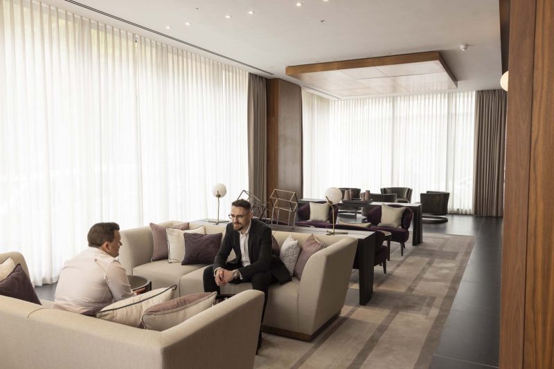 Two men in business attire meeting in a modern, well-lit lounge.