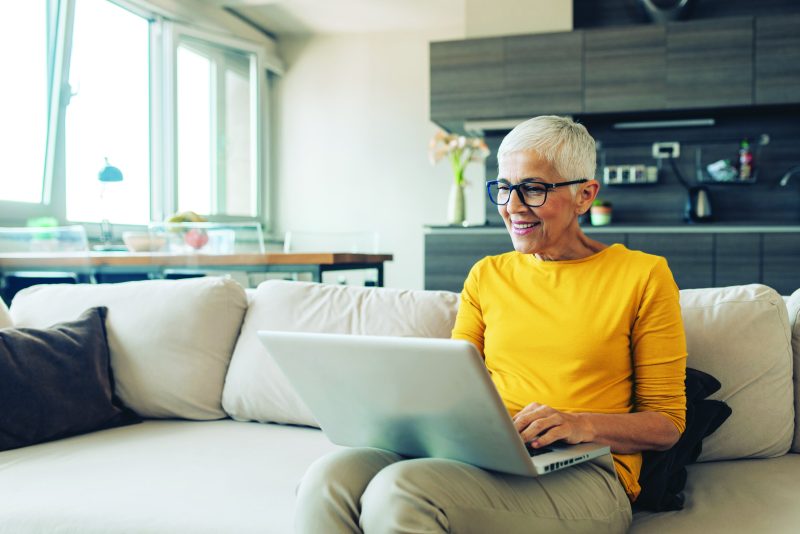 Woman working on laptop from home sofa.
