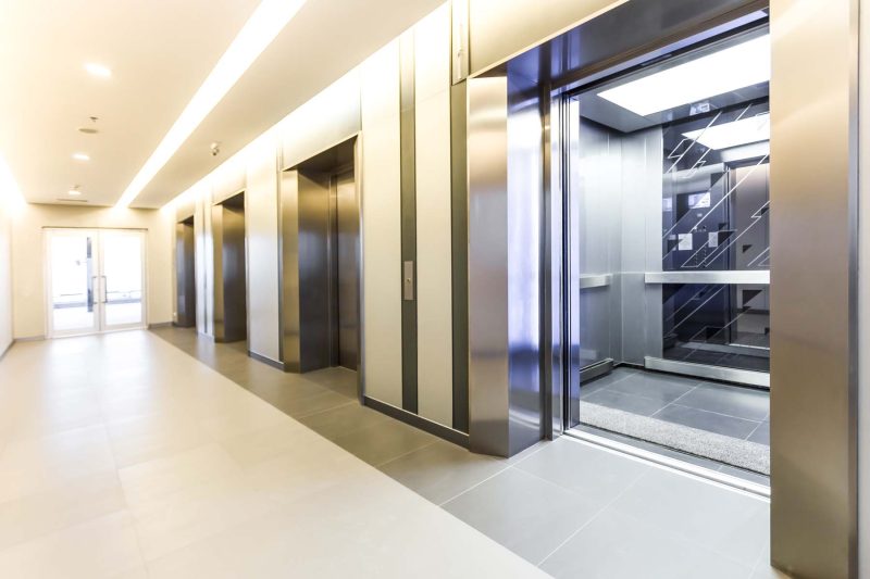 Three modern steel elevator cabins in a building lobby.