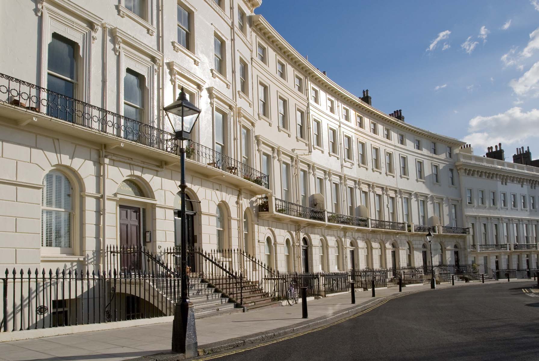 Curved row of elegant, white townhouses on a sunny street.