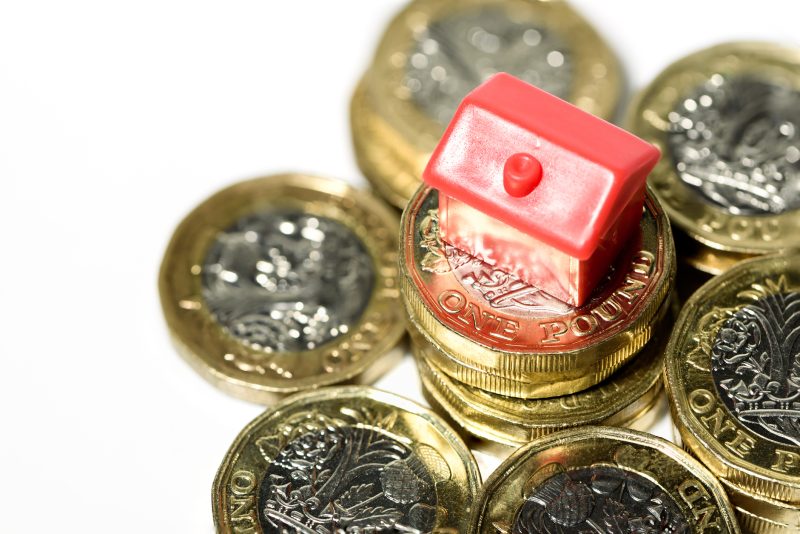 Red miniature house on a stack of British one-pound coins.