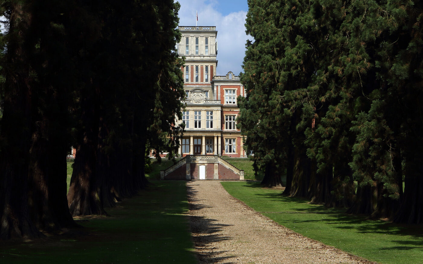 Grand building viewed through tall trees, gravel path leading to entrance.