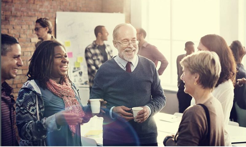 Group of people conversing and smiling, holding coffee cups.