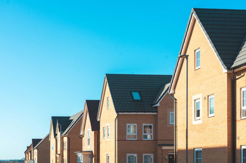 Row of tan brick townhouses under a blue sky.