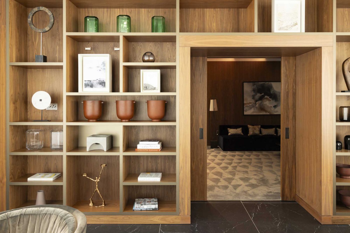 Stylish wooden shelving unit with décor and books, leading to a lounge area.