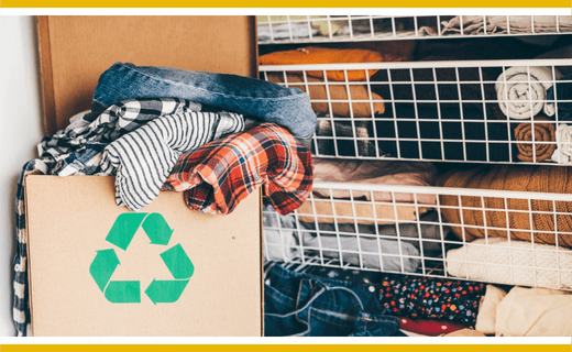 Clothes recycling box with recycling symbol; clothes in background.