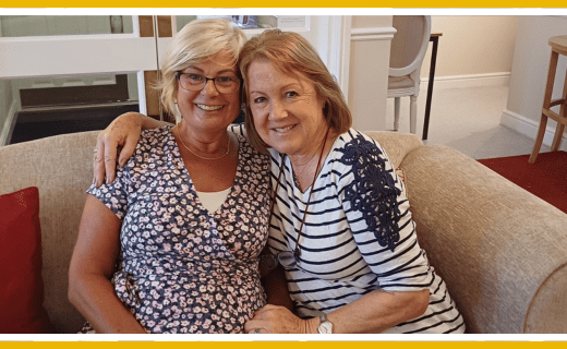 Two women smiling, sitting together on a sofa.