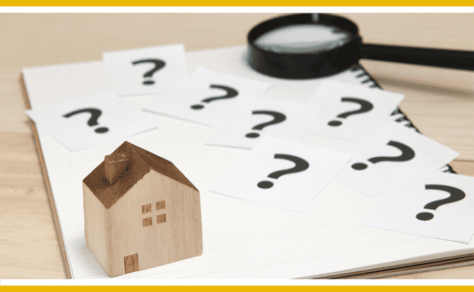 Wooden house model on notepad with question marks and magnifying glass.
