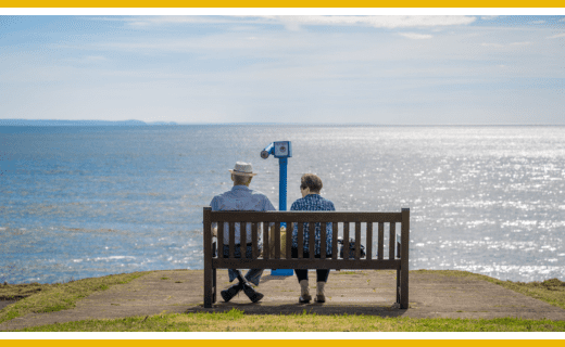 Senior couple sitting on a bench overlooking the sea.