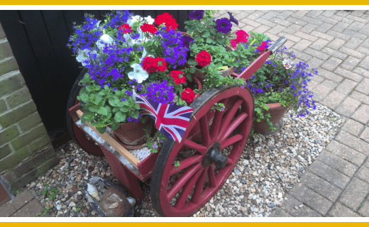 Red wheelbarrow filled with colorful flowers and a small Union Jack flag.