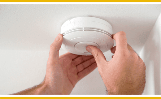 Hands installing a smoke alarm on a ceiling.
