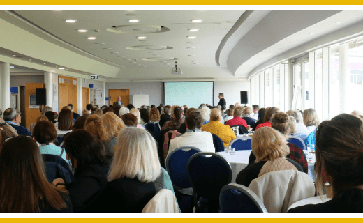 Large conference room; audience listening to presentation.