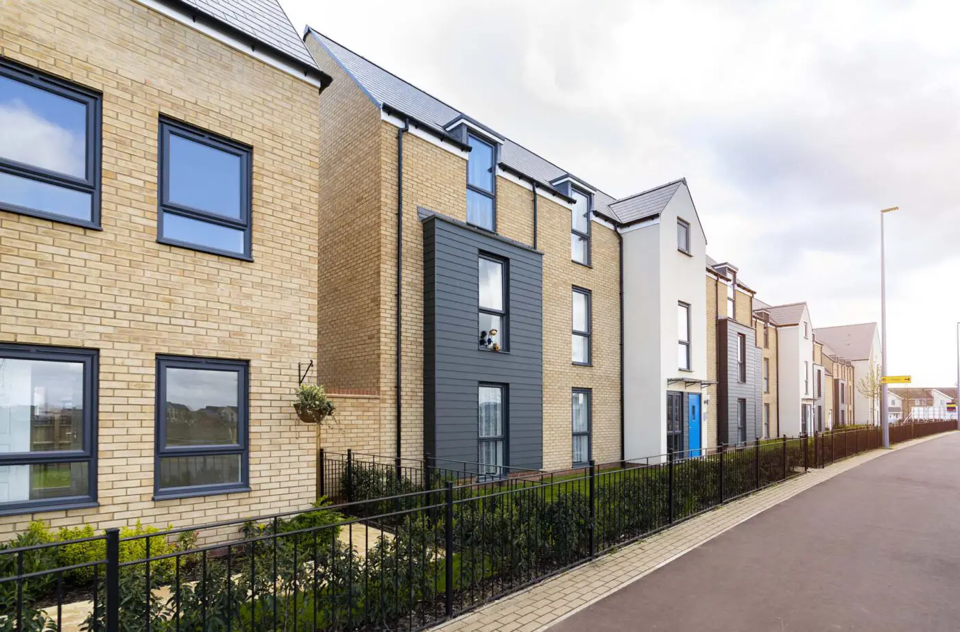 Row of new homes with black fences and paved walkway.